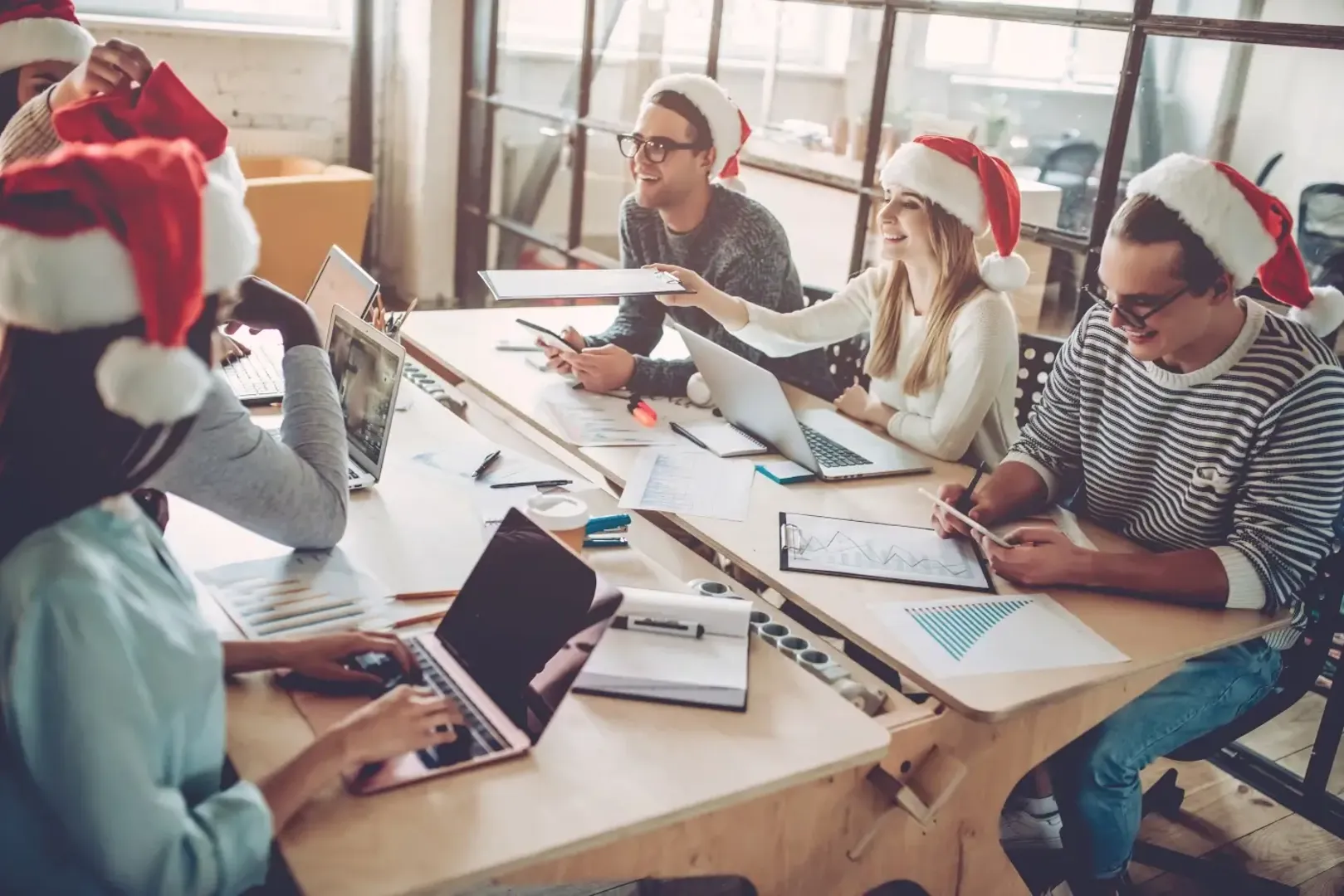 People wearing Santa hats engaged in work on laptops, creating a cheerful atmosphere.